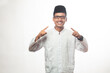 Asian Muslim man with glasses, brown skin, smiling facing the camera and both hands pointing forward, Muslim man wearing koko shirt. white isolated
