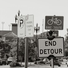 Grayscale Shot Of Various Street Signs Like Bike Route And End Detour On A Road