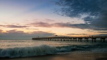 A Pier With Waves Crashing Over The Shore During The Sunset