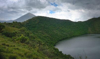 Wall Mural - Majestic lake lies in the valley between grassy rolling hills, surrounded by a lush forest.