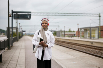 Young smiling woman wearing hijab standing at train station
