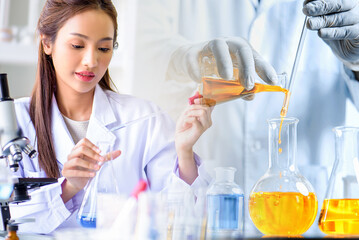 Wall Mural - Attractive scientist woman looking chemical sample in flask at laboratory with lab glassware background. Science or chemistry research and development concept.	
