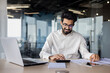 © Tetiana - Indian young male accountant, financial analyst and auditor working focused in office at desk with documents and calculator