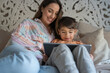 Mother and son (6-7) using digital tablet in bedroom