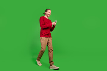 Poster - Full length photo of intelligent guy wear red sweatshirt hold smartphone read email go empty space isolated on green color background