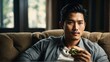 An handsome asian man relaxing on the sofa and eating a sandwich from Generative AI