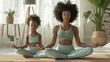 A woman and a young girl are sitting cross-legged on mats in a meditative pose with eyes closed, practicing yoga in a serene indoor environment.