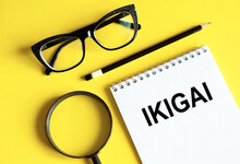 IKIGAI. The Word Ikigai On Notebook And Pencil, Magnifier And Eyeglasses On Yellow Background. IKIGAI Is A Japanese Concept Reason For Being Of Life Purpose.