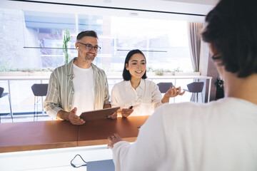 Fototapete - Happy Caucasian man in optical spectacles for vison correction and Asian female colleague smiling at reception during corporate collaboration, successful employees with digital touch pad feeling good