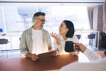 Fototapete - Happy Caucasian man in optical eyewear for vison protection and Asian female colleague smiling at reception during corporate collaboration, successful employees with digital touch pad talking