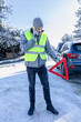 © zphoto83 - Driver calling roadside assistance while placing warning triangle on the road. Car in the background. Winter scene.
