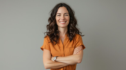 Sticker - a cheerful young woman with long wavy hair, wearing an orange blouse, standing with her arms crossed against a neutral gray background