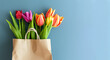 Bouquet of tulips in a gift bag on a blue background. Concept for international women's day, Valentine's day and romantic anniversaries. Copy space. Banner.