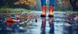 © AkuAku - A person with orange rain boots stands in a puddle, water splashing as their foot sinks into the wet asphalt.
