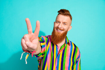 Photo of cheerful satisfied positive glad man wear trendy colorful striped clothes show two fingers v-sign isolated on cyan color background