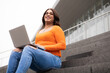 © Alberto - Trans woman student looking to the camera and using laptop in university stairs.