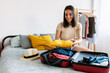 © Xavier Lorenzo - Happy young woman preparing luggage before summer travel vacation or weekend getaway. Packing preparation before holiday departure