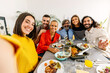 © Xavier Lorenzo - Group of multi-generational family enjoying dinner party taking selfie portrait sitting together at living room table.