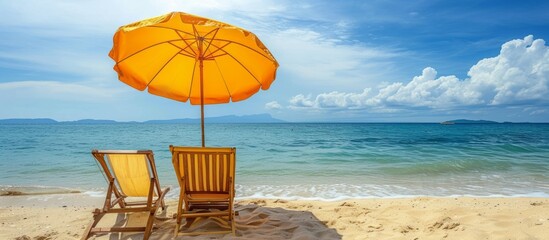 Wall Mural - On the sandy beach, you'll find two chairs, an umbrella providing shade, and a picturesque view of the water, sky, clouds, and natural landscape.