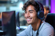 © Gayan - Smiling young man with headphones using computer in a modern office setting.