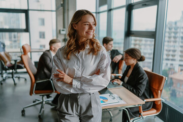 Smiling female entrepreneur with crossed hands standing in office on colleagues background