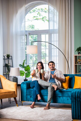 Wall Mural - Cheerful young beautiful Indian couple having coffee together on sofa at home..