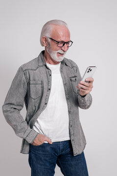 Portrait of confident old businessman with hand in pocket using smart phone over white background