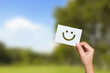 © sichon - Service rating, feedback, satisfaction concept. Hand holding white paper with smile emoticon for rating feedback scale on nature background