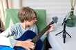 © Viktoriia - Young teenage boy streaming video online for social media blog or webinar, while playing guitar, making online music lesson, teenagers in cyberspace concept