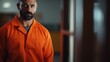 A man wearing an orange prison uniform stares directly into the camera. This image can be used to depict themes of incarceration, criminal justice, or law enforcement