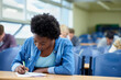© Katie/peopleimages.com - Writing, university and black woman student in classroom studying for test, exam or assignment. Education, college and female person working on project with knowledge in lecture hall for learning.