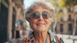 Elegant older woman with gray hair wearing large round sunglasses a colorful floral blouse and large turquoise earrings smiling and looking directly at the camera.