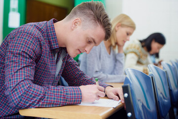 Canvas Print - University student, desk and writing exam in classroom for education assessment for knowledge, diploma or scholarship. Men, woman and test in London lecture hall or study document, academy or college