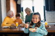© Dorde - Adorable girl feeling happy while eating her favorite breakfast corn flakes cereals with milk in the morning standing in the kitchen with grandmother, grandfather and a sibling. Focus is on the girl.