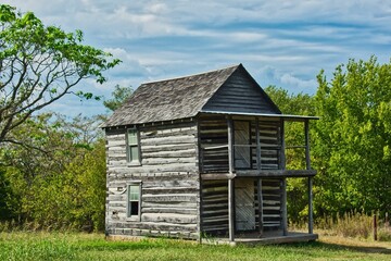 Poster - Aged wooden log house situated in a sprawling grassy meadow.