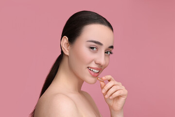 Poster - Beautiful young woman with vitamin pill on pink background