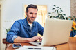 © baranq - Adult man working remotely at home office using laptop