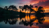Fototapeta Zachód słońca - Frame the stark contrast between the dark silhouettes of the trees against the vibrant hues of the sunset sky and capturing the magical moment when day meets night at the edge of the serene lake