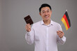 Immigration. Happy man with passport and flag of Germany on grey background, space for text