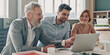 © gstockstudio - Three confident business people looking at laptop and smiling while working in the office together