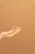 © Pavel - Lady's arm with a drop of cosmetic cream on the top of the finger on a beige background, Groomed hands, natural short nails, on a peach backdrop. Vertical photo. Ads