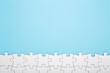 Row of completed different white puzzle pieces on light blue table background. Pastel color. Closeup. Empty place for text. Top down view.