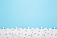 Row Of Completed Different White Puzzle Pieces On Light Blue Table Background. Pastel Color. Closeup. Empty Place For Text. Top Down View.