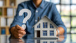 Une personne tenant un point d'interrogation dans sa main avec une maison miniature.