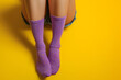 Beautiful legs of a young girl with long purple stylish socks isolated on yellow empty background with space for text or inscriptions
