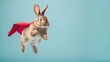 Superhero Bunny, Cute bunny with a red cloak jumping and flying on light blue background with copy space. The concept of a superhero, super bunny, leader, funny animal studio shot. 