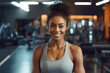 © Galina - Attractive black woman in sportswear stands against the backdrop of a gym and exercise equipment. Personal trainer in a sports club smiles and looks at the camera.