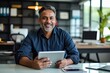 © alauli - Indian middle aged business man ceo professional investor smiling happily using tablet computer, looking at camera on desk in office