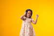 Smiling kid girl with headphones enjoying music and dancing on yellow background. Lifestyle and leasure concept
