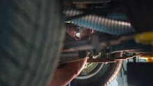 Blurry Image Capturing The Hands Of A Car Mechanic As They Tighten A Nut On The Underbelly Of A Vehicle In A Service Bay